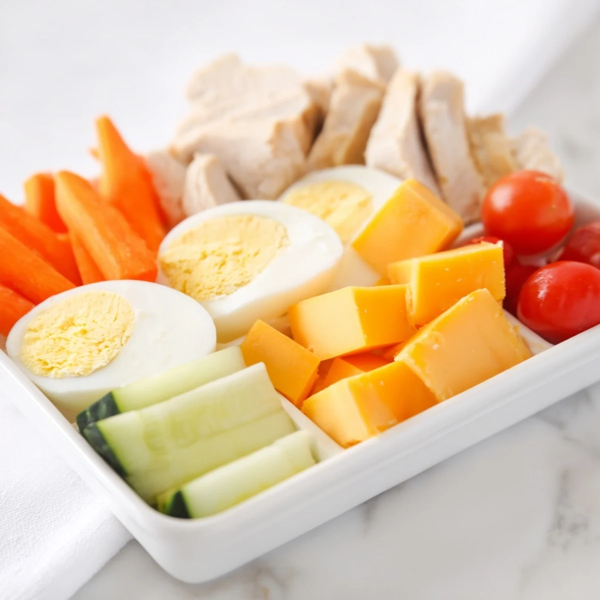 Protein snack boxes arranged, showcasing sliced chicken, fresh veggies, and hummus for easy snacking.