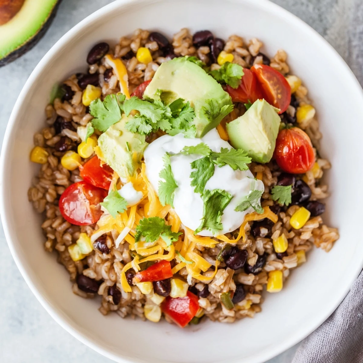 An easy homemade Brown Rice Burrito Bowl with layers of seasoned beans, corn, cherry tomatoes, and cheese, ready for a weeknight dinner.