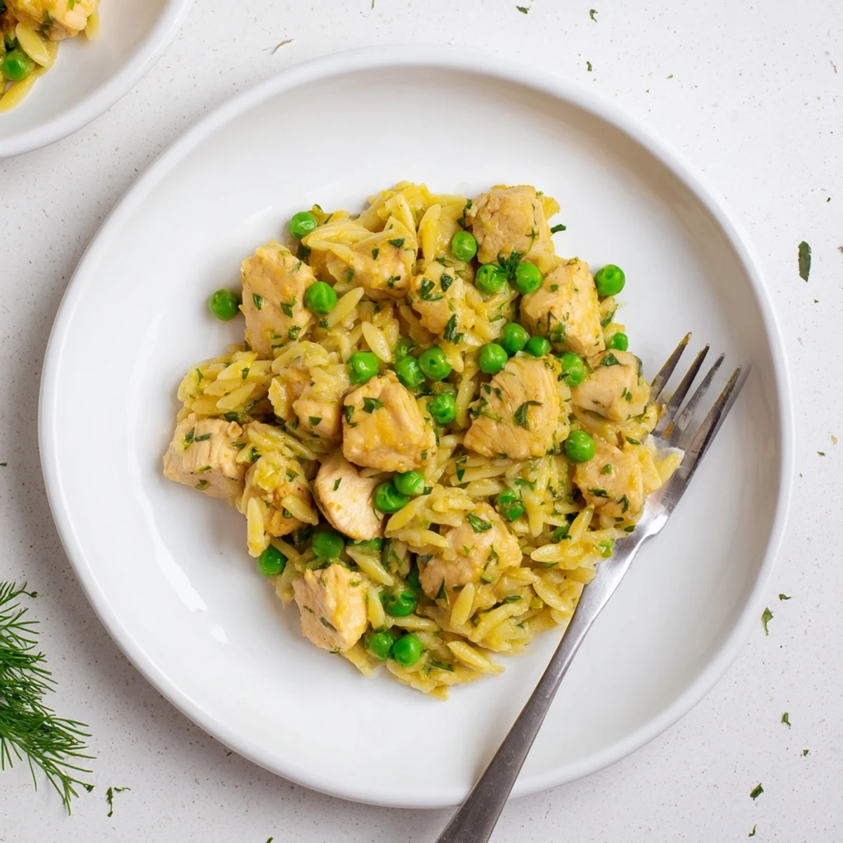 Golden-brown chicken pieces nestled in creamy orzo pasta, with vibrant green peas and fresh herbs in a bright lemon sauce, served in a rustic skillet.