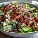 Colorful Greek salad bowl featuring juicy grilled chicken, crisp cucumbers, and tangy olives, drizzled with zesty lemon dressing.  