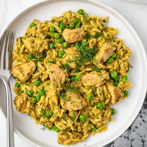 A close-up of tender herb-crusted chicken and orzo pasta simmering in a zesty lemon broth, with a garnish of fresh parsley and dill for a spring dinner.