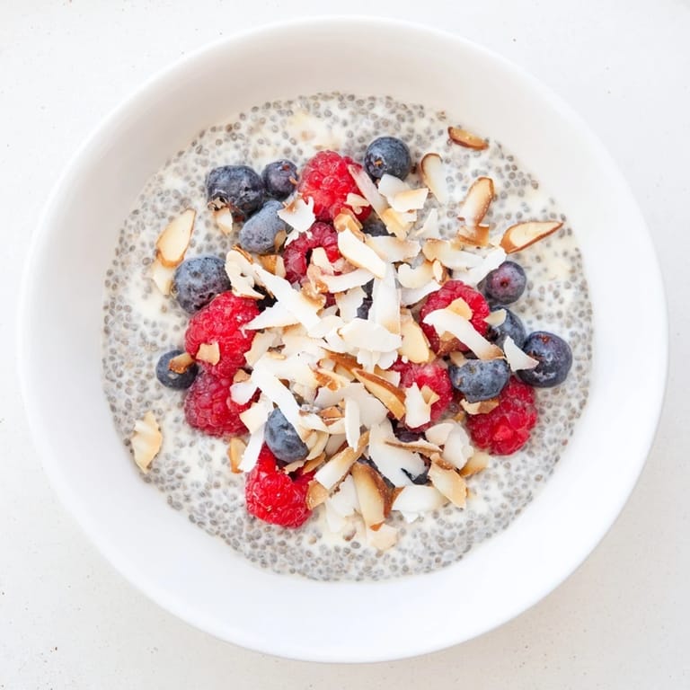 A close-up of Poppy Seed Chia Pudding topped with raspberries, coconut flakes, and a drizzle of honey.  