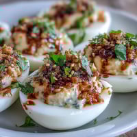 A close-up of Spicy Chili Garlic Deviled Eggs, with creamy yellow filling and a glossy red chili oil drizzle on top.
